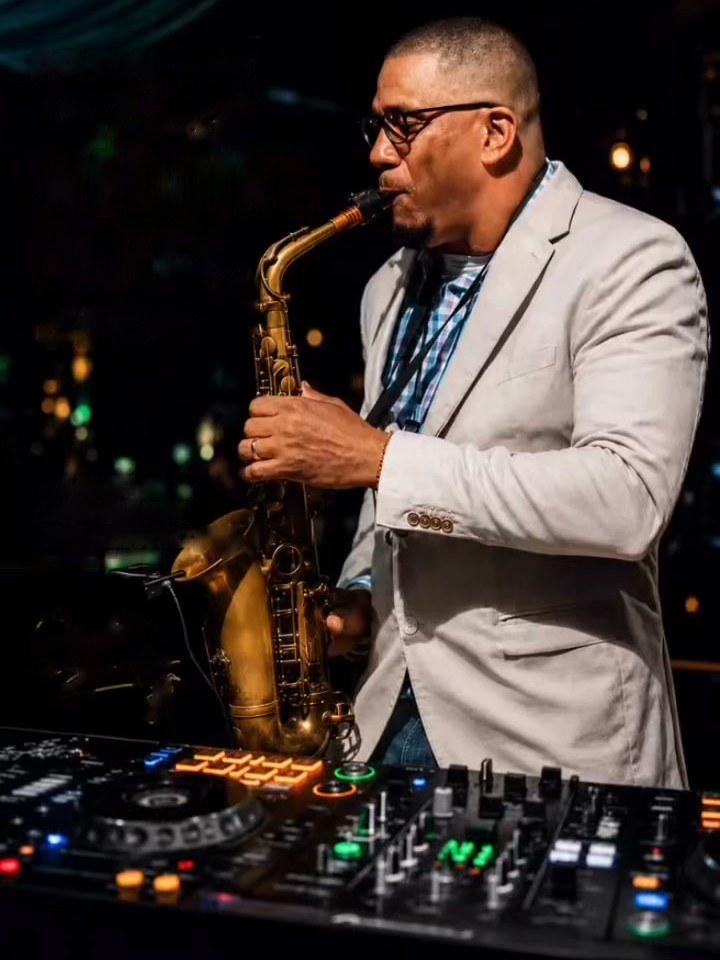 Carlos Alberto Mora Baez playing saxophone over a DJ controller